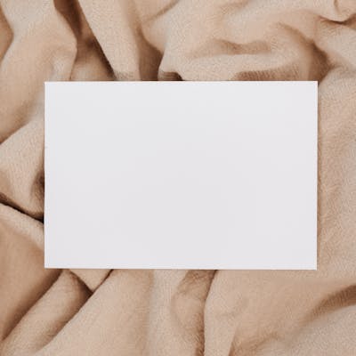 A blank white card on beige textured fabric offering space for text or design.