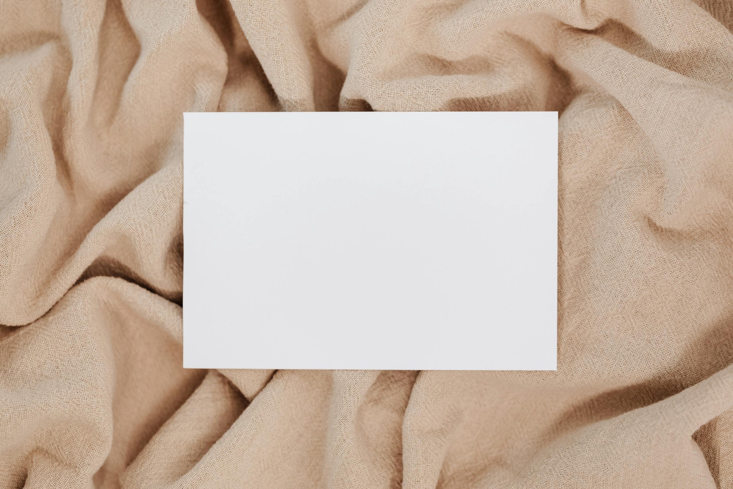 A blank white card on beige textured fabric offering space for text or design.