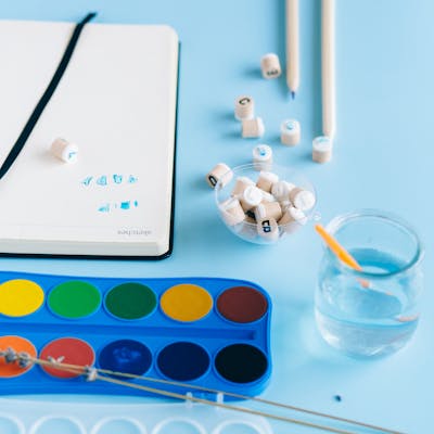 A collection of art supplies with watercolor paints on a blue surface.