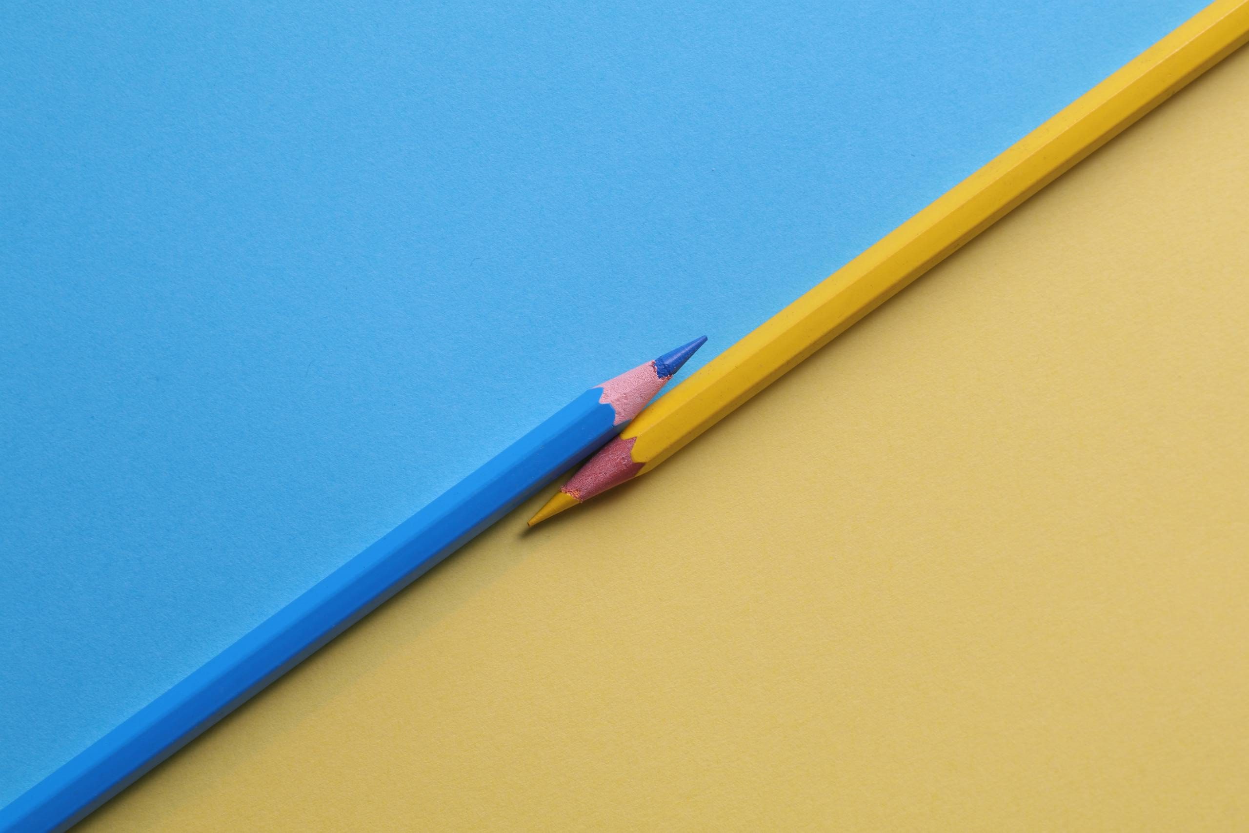 Close-up of vibrant yellow and blue colored pencils on contrasting paper backgrounds.