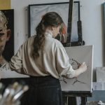 Female artist working on a canvas in a studio with paintings in the background.