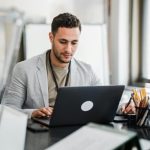 Focused man working on a laptop in a modern office setting, emphasizing productivity and technology.