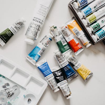 Top view of vibrant acrylic paint tubes and palette on a white surface.