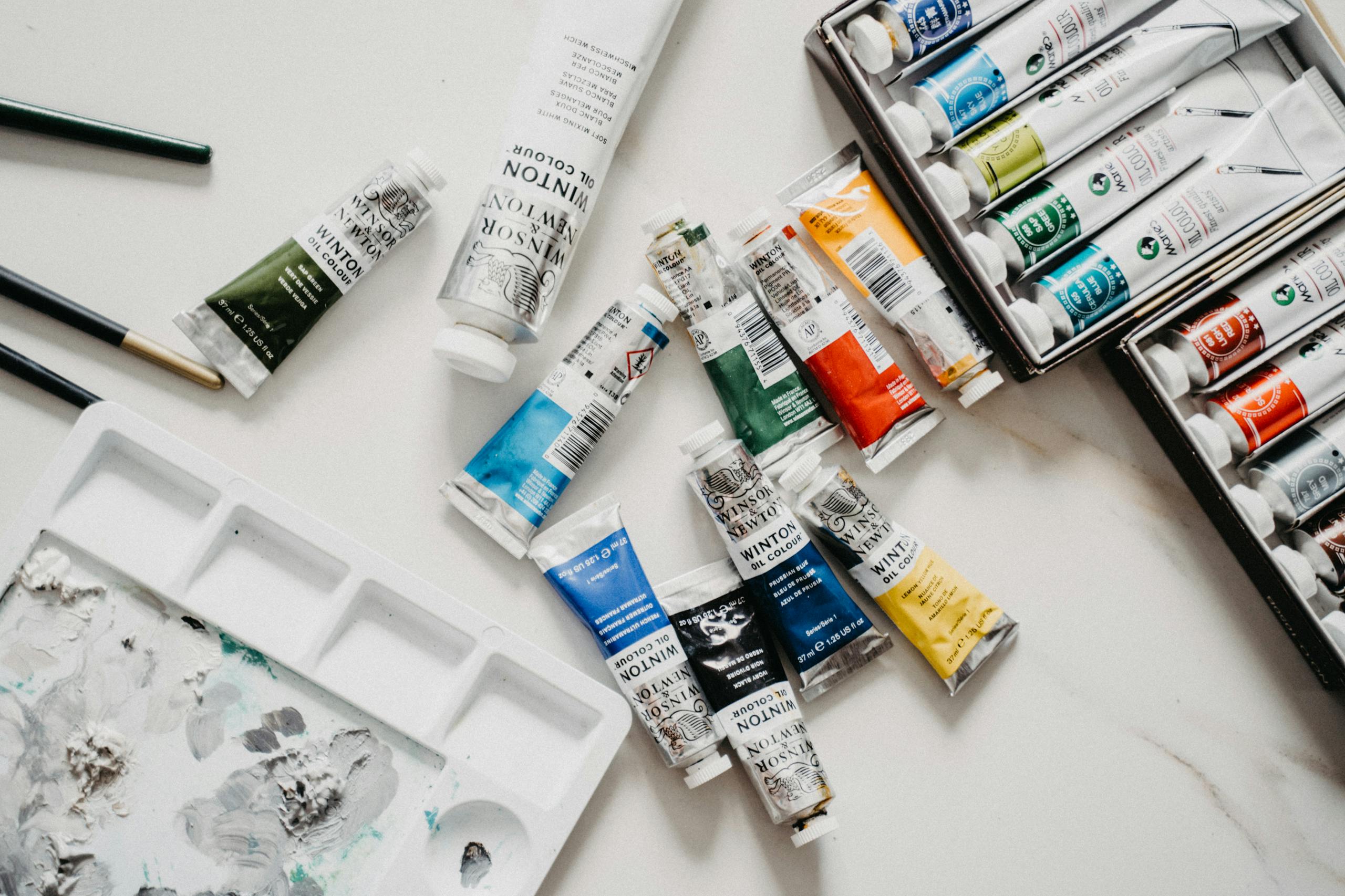 Top view of vibrant acrylic paint tubes and palette on a white surface.