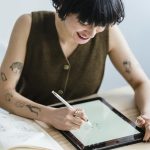 Young female artist drawing digitally with stylus, showcasing creativity in modern workspace.